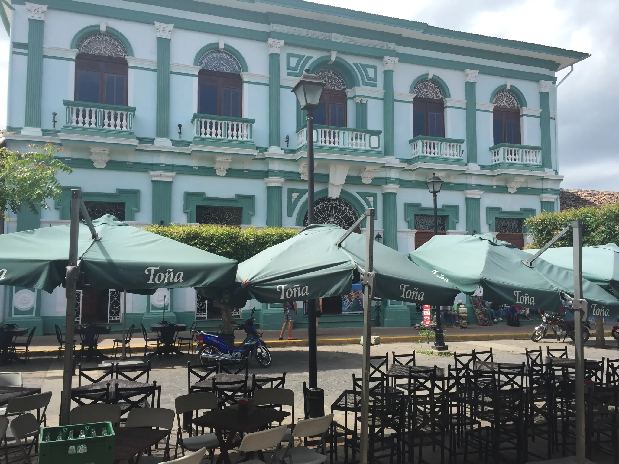 Granada Nicaragua central park with Toña beer umbrellas at outdoor cafe tables — colonial building