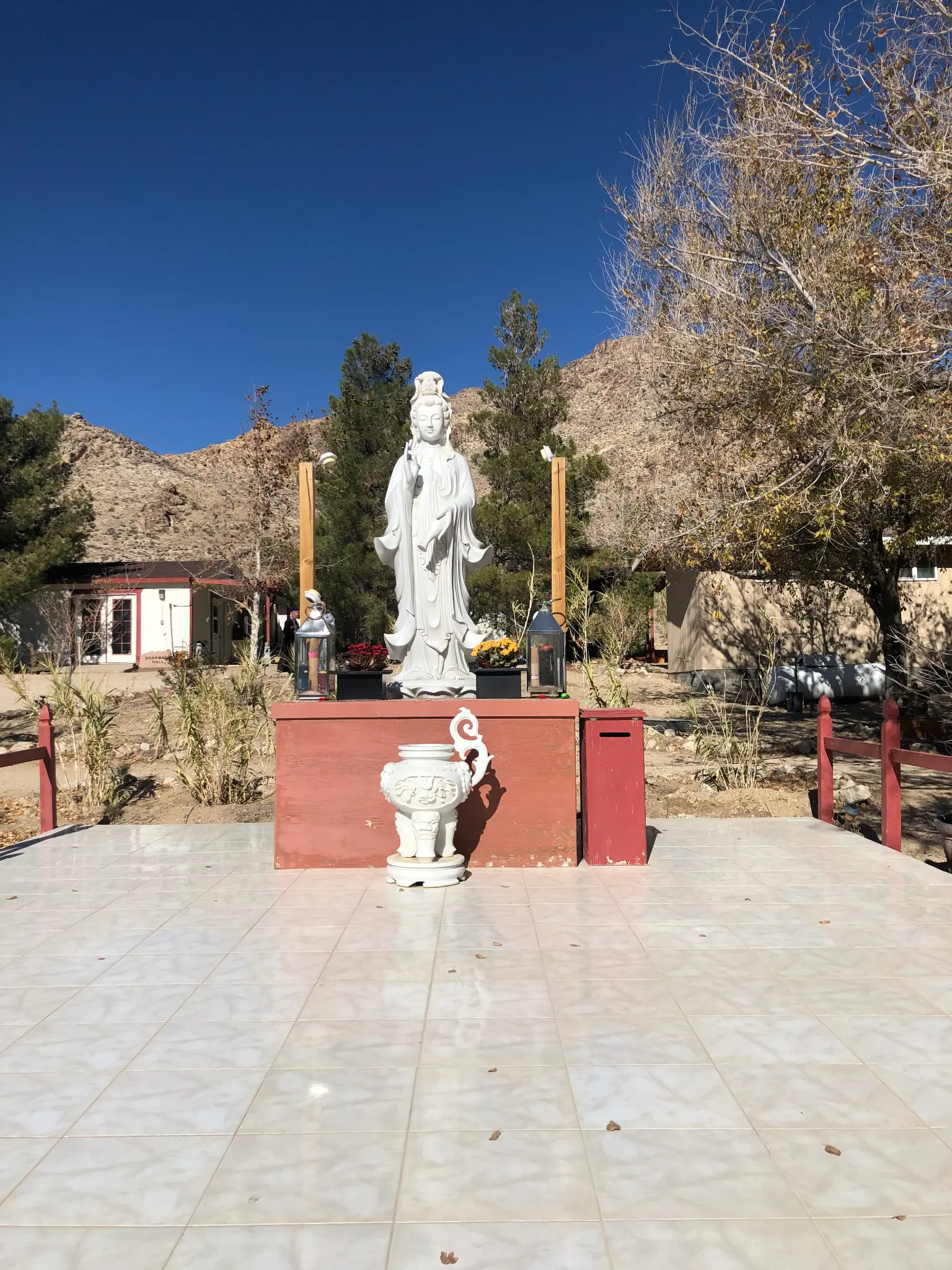 Guanyin statue at the Buddhist temple in Lucerne Valley β white bodhisattva figure on a red altar against desert mountains and blue sky