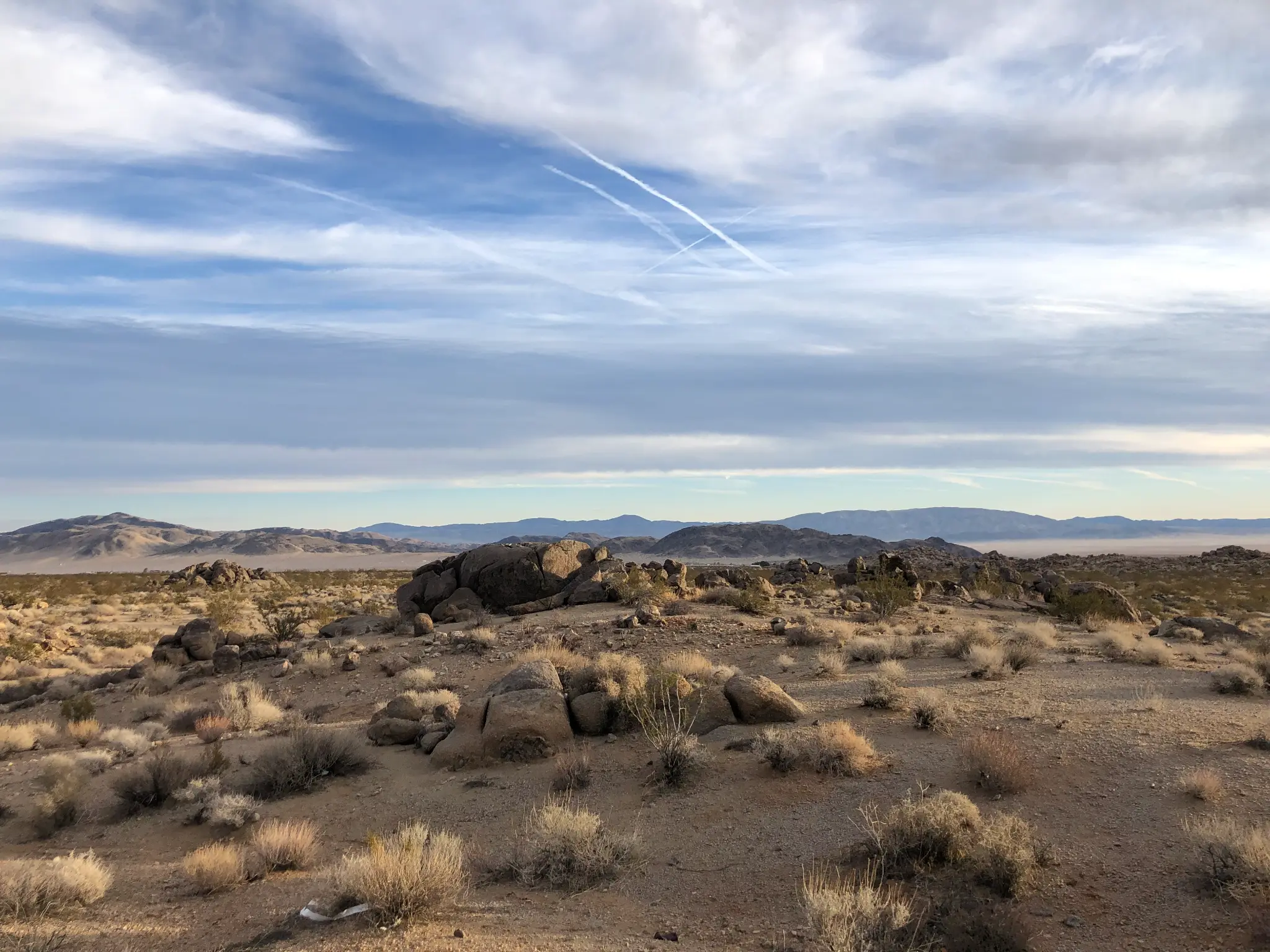 Wide Mojave desert panorama near Landers, CA β granite boulders, desert scrub, and mountain ranges under a dramatic cloud-streaked sky