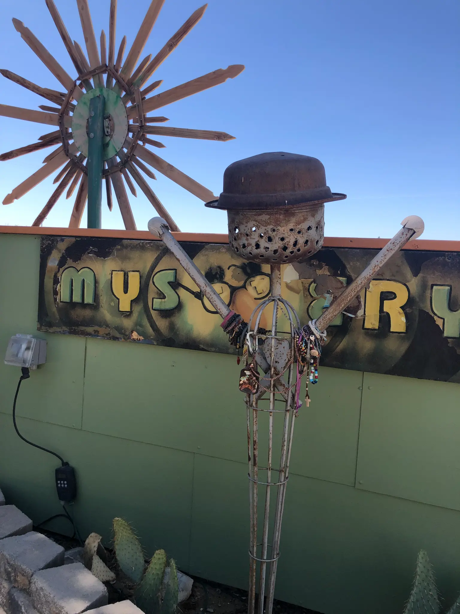 Whimsical metal sculpture with a bowler hat and outstretched arms in front of a Mystery sign at the Integratron grounds