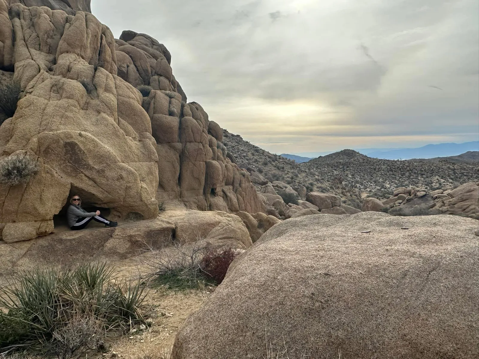 Kristen Shepherd sitting inside a rock alcove in the desert, looking out at the vast landscape โ Joshua Tree, California