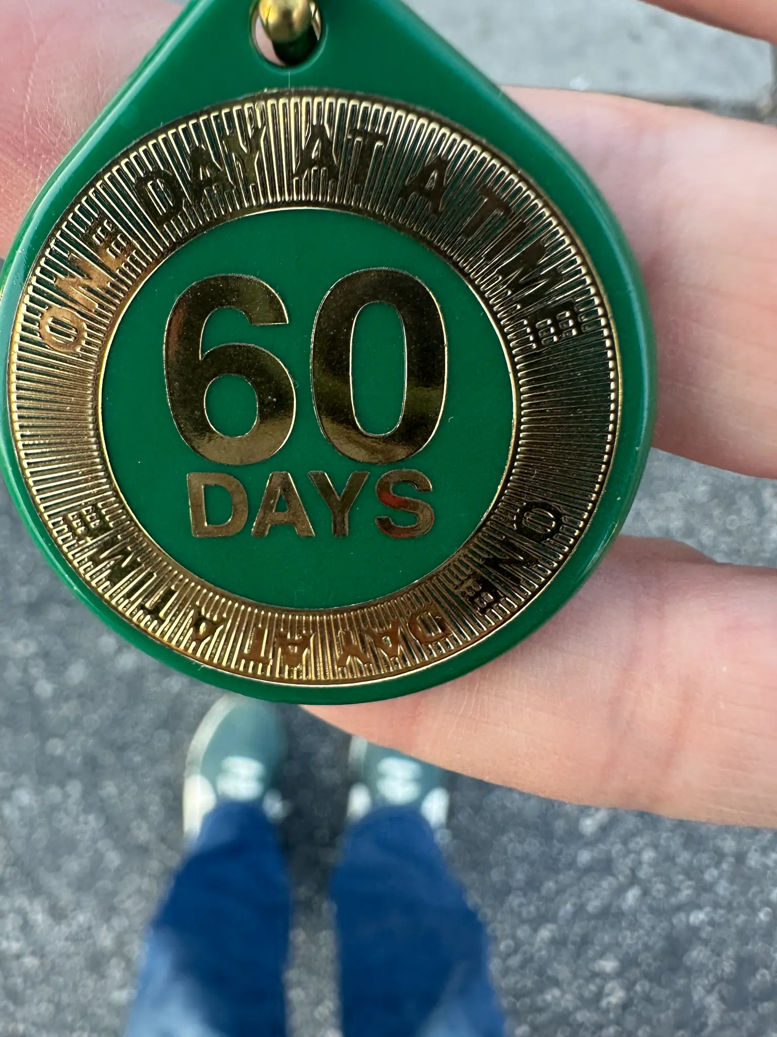 Kristen's 60-day sobriety chip — green and gold, held in her hand